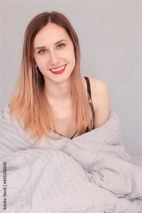 Portrait Of Pretty Redhead Woman In Black Lingerie On Bed With Grey Sheets And Blanket Stock