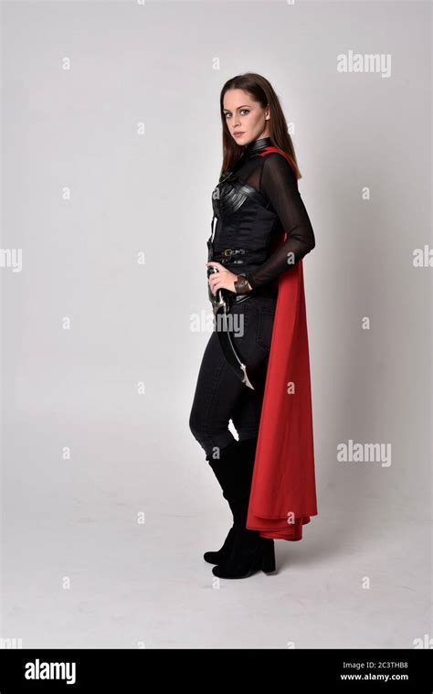 Portrait Of Brunette Girl Wearing Black Leather Catsuit Red Cloak Full Length Standing Pose