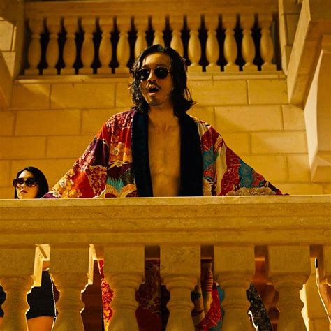 A Man Wearing Sunglasses And A Robe Standing On A Balcony