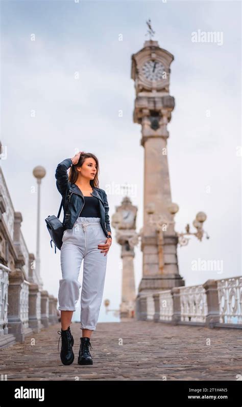 Lifestyle In The City With A Blonde Girl In White Pants And A Leather Jacket Walking Down A