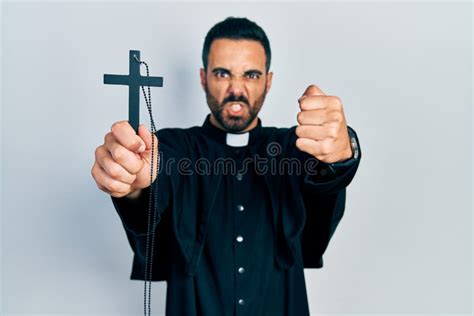 Handsome Hispanic Priest Man With Beard Holding Catholic Cross Annoyed