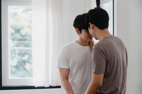 Couple gay asiatique debout et étreignant près de la fenêtre à la maison Les jeunes LGBTQ