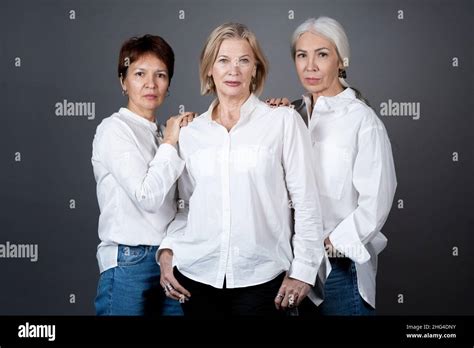 Portrait Of Beautiful Mature Women In White Shirts Posing At Camera Against The Grey Background