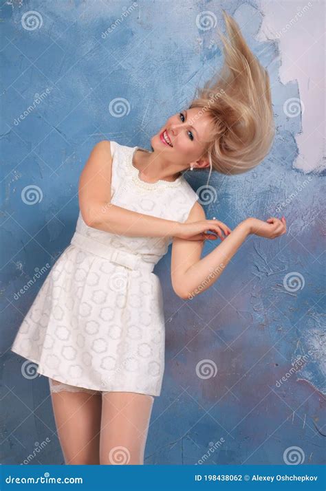 Blonde Long Legged Model In White Minidress And White Stockings Posing In Studio Stock Photo