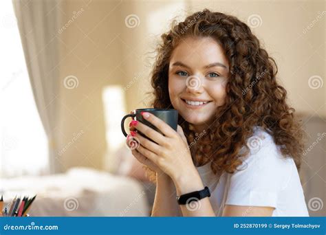 Young Curly Haired Woman Relaxing Indoors At Home With Cup Of Coffee