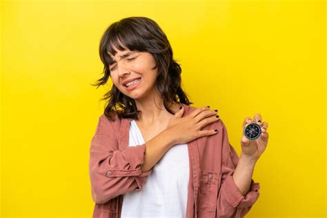 Jovem mulher latina segurando bússola isolada em fundo amarelo sofrendo de dor no ombro por ter