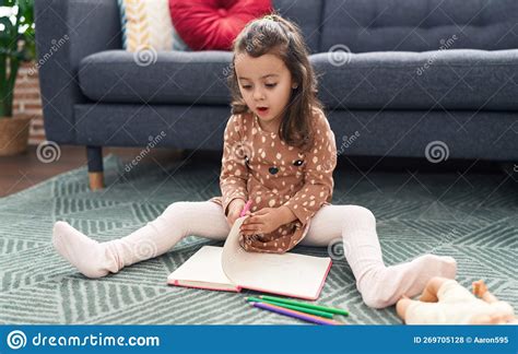 Adorable Hispanic Girl Sitting On Floor Drawing On Notebook At Home