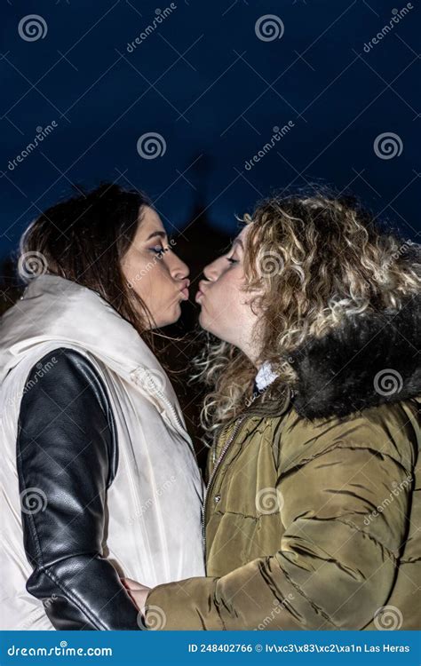 A Lesbian Couple Kissing Each Other With Puckering Lips At Night In The Outdoors Stock Photo