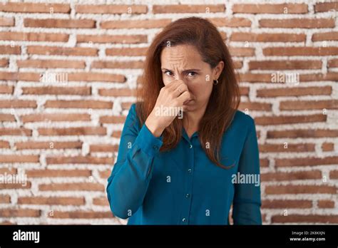 Brunette Woman Standing Over Bricks Wall Smelling Something Stinky And Disgusting Intolerable
