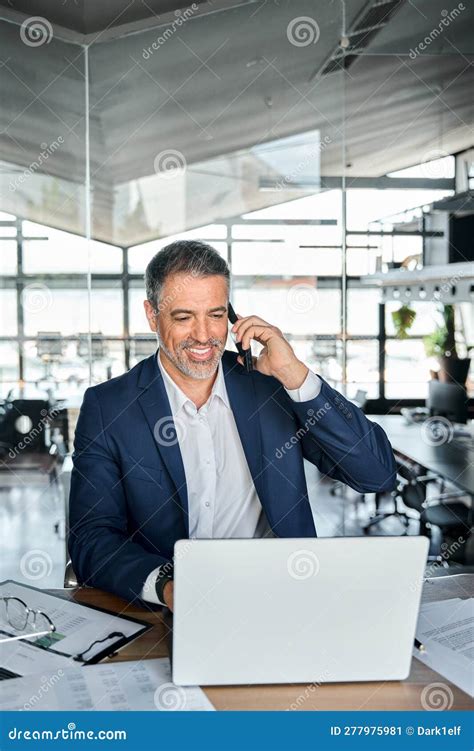 Happy Middle Aged Business Man Making Phone Call Using Laptop In Office