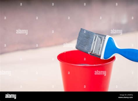 Paint Brush And A Bucket With Paint Next To A Building Exterior Wall
