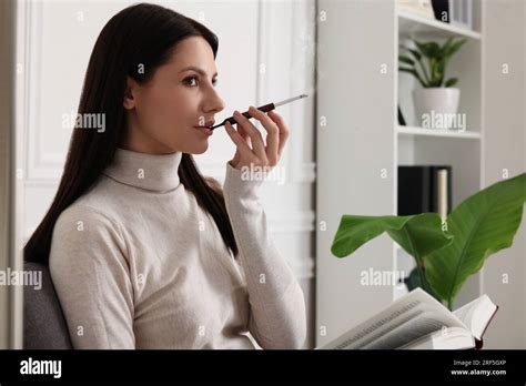 Woman Using Cigarette Holder For Smoking While Reading Book Indoors