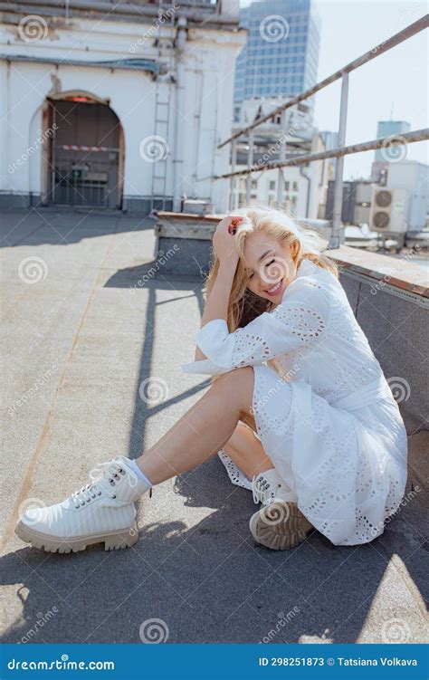 Positive Emotions Feminine Blonde With Long Loose Hair Smiling Sitting On Roof Of City