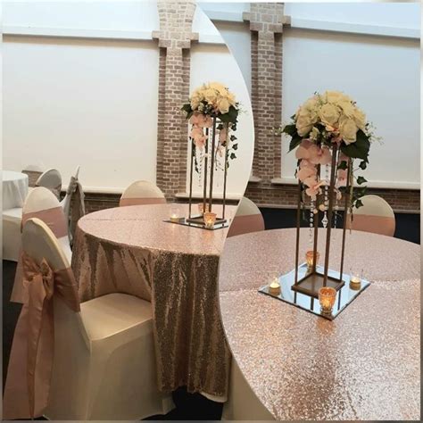 Two Tall Vases Filled With Flowers Sit On Top Of A Round Table Covered