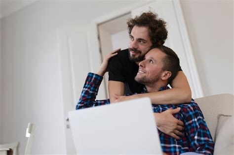 Lindo casal gay rindo juntos enquanto está sentado em sua sala de estar em casa Dois românticos