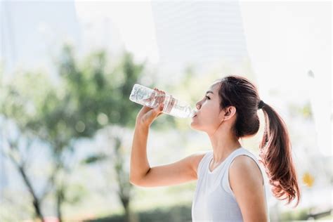 Agua potable joven asiática de la botella de agua después de correr en