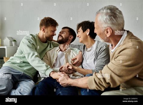 A Gay Couple Sits On A Couch With Parents Smiling And Holding Hands Stock Photo Alamy