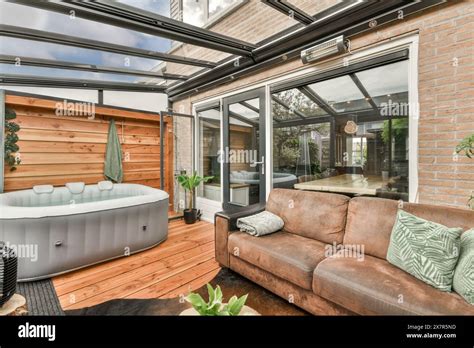 Elegant Conservatory Space Enclosed With Glass Panels Featuring A Luxurious Hot Tub And A Plush