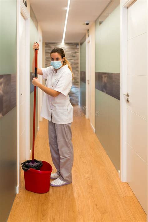 Woman Standing Holding Mop In A Bucket Looking At Camera In Hallway Of