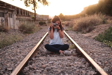 Chica joven viajera sentada en las vías del tren haciendo fotos wall