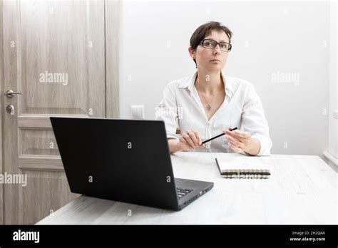Middle Aged Woman With Short Haired Brunette In Glasses Works At A Laptop Near Window Office