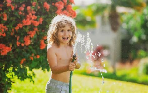 Un niño adorable regando las plantas con un rociador de manguera con