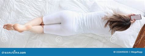 Woman Lying On Her Stomach In Bed And Looking At Phone Tip View Stock