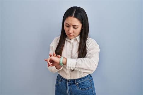 Joven Mujer Latina De Pie Sobre Fondo Azul Comprobando La Hora En El Reloj De Pulsera Relajada Y