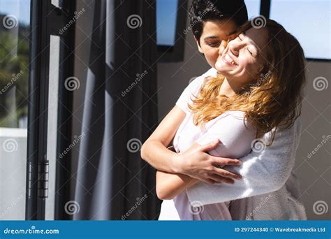 Happy Biracial Lesbian Couple Embracing In Sun By Window At Home Copy Space Stock Photo Image
