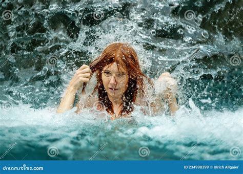 Beautiful Redhead Woman In Bikini Under The Splashing Water Shower Of The Waterfall In The Spa