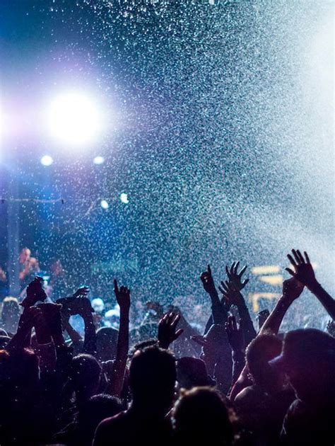 A Crowd At A Concert With Their Hands In The Air And Water Spraying All