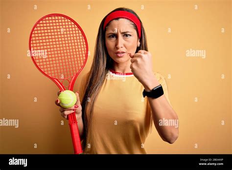 Belle brunette sportswoman jouant au tennis avec raquette et boule sur fond jaune agacé et