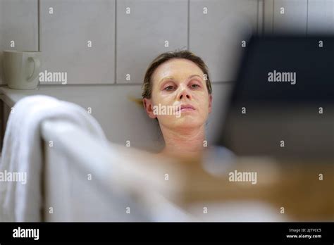 Woman Relaxing In A Hot Bath Reading On A Tablet Or Smartphone With Focus To Her Face Stock