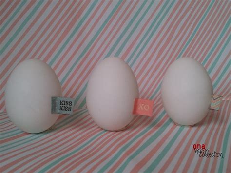 Three Eggs With Labels On Them Sitting On A Striped Table Cloth One Is