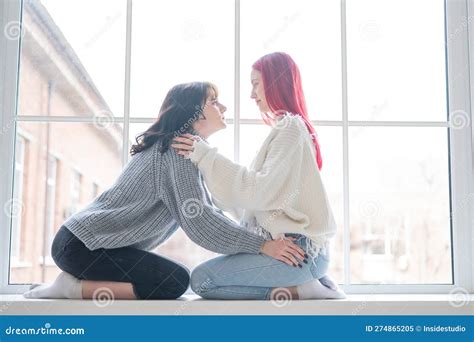 Two Women Dressed In Sweaters Sit By The Window And Gently Hug Lesbian Intimacy Stock Image