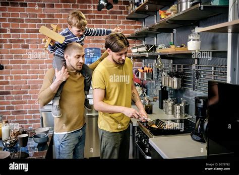 Jeune homme gay cuisant le petit déjeuner sur la cuisinière dans la cuisine quand son mari donne