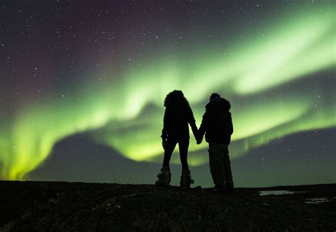 Two People Holding Hands In Front Of An Aurora Bore And The Sky With