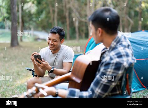 Lgbtqia Gay Couple Camping Together In Woods For Holidays And Relax On Guitar Together Stock