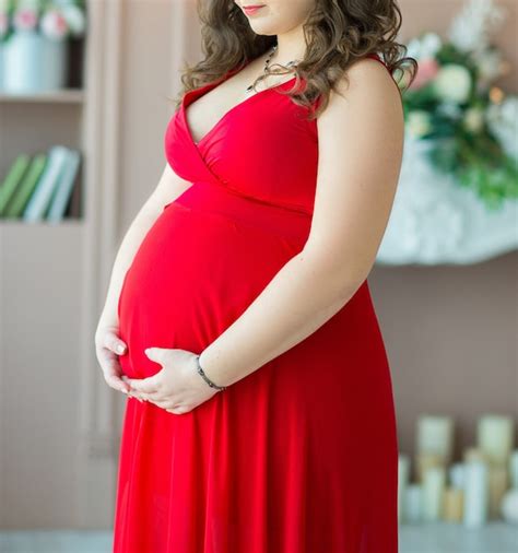 Premium Photo A Pregnant Woman With Dark Hair In A Red Dress Hugs Her Big Belly Tenderly With