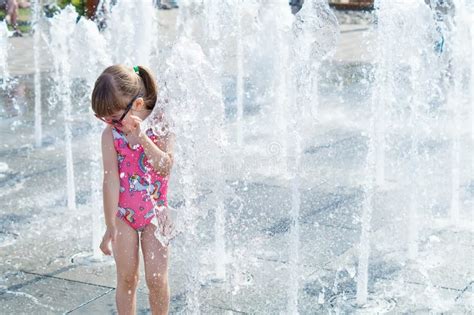 A Little Girl is Playing in the Fountain Jets on a Hot Summer Day. a ...