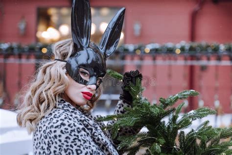 Blonde Woman In Coat And Black Bunny Mask Easter Bunny Concept Naughty Girl Stock Photo
