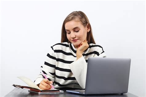 Eine junge blonde Frau in einem weißen Pullover ist gelangweilt vom Lernen während sie mit