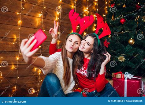 Two Smiling Young Women In Christmas Decorations Taking A Selfie With