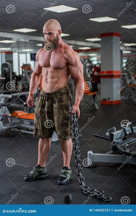 A Bald Bearded Bodybuilder With Large Relief Muscles Holds A Heavy