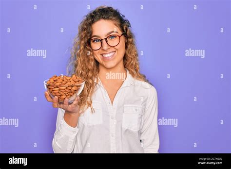 Junge schöne blonde Frau mit blauen Augen halten Schüssel mit gesunden Mandel Snack mit einem