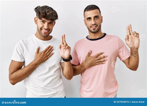 Joven Pareja Gay Parado En Un Entorno Aislado Sonriendo Jurando Con La Mano En El Pecho Y Los