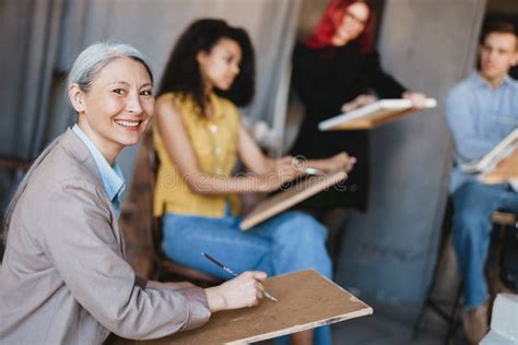 Mature Teacher Drawing With Her Students During Class In Art School