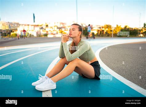 Tired Upset Female Athlete Sitting On Running Track Resting After