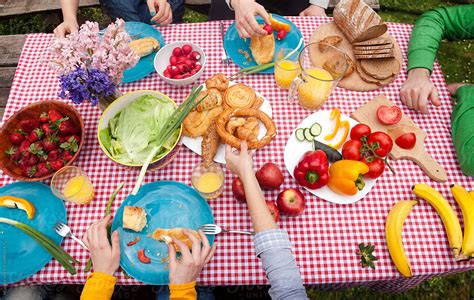 People Sitting Around The Table Full Of Picnic Food And Eating By