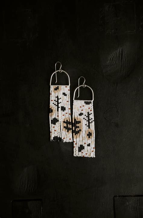 Pair Of Beaded Earrings Hanging From Hooks On Black Wall With White And